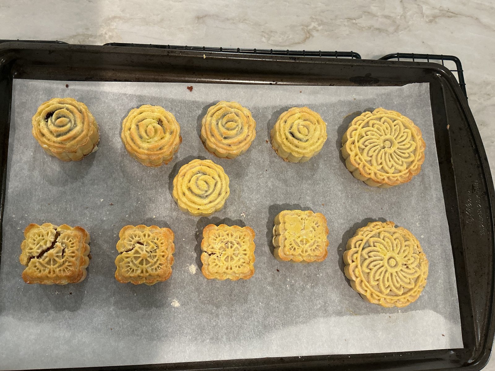 A tray of golden baked mooncakes in several decorative shapes